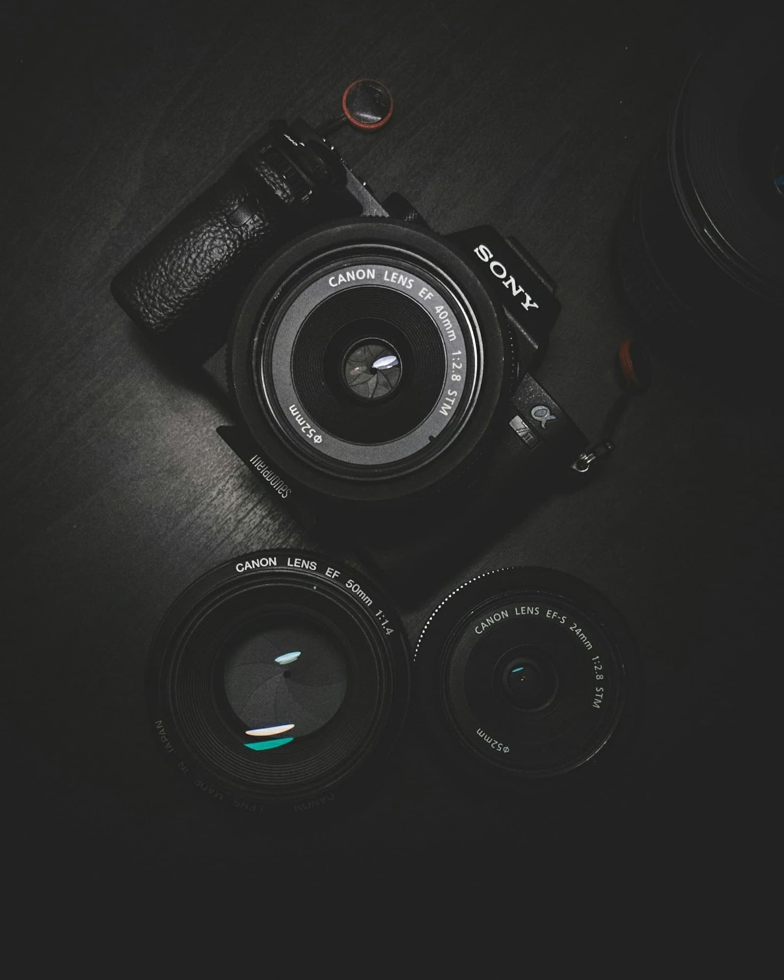 A mirrorless camera body and three prime lenses laid out on a dark surface